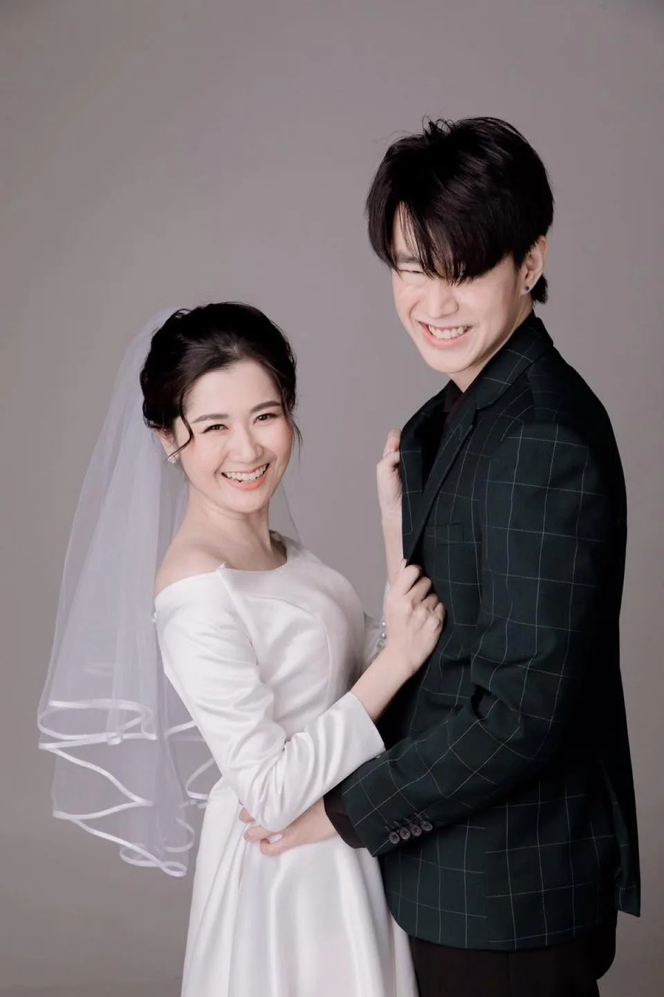 คู่บ่าวสาวยิ้มในชุดแต่งงานและสูทสีเข้ม