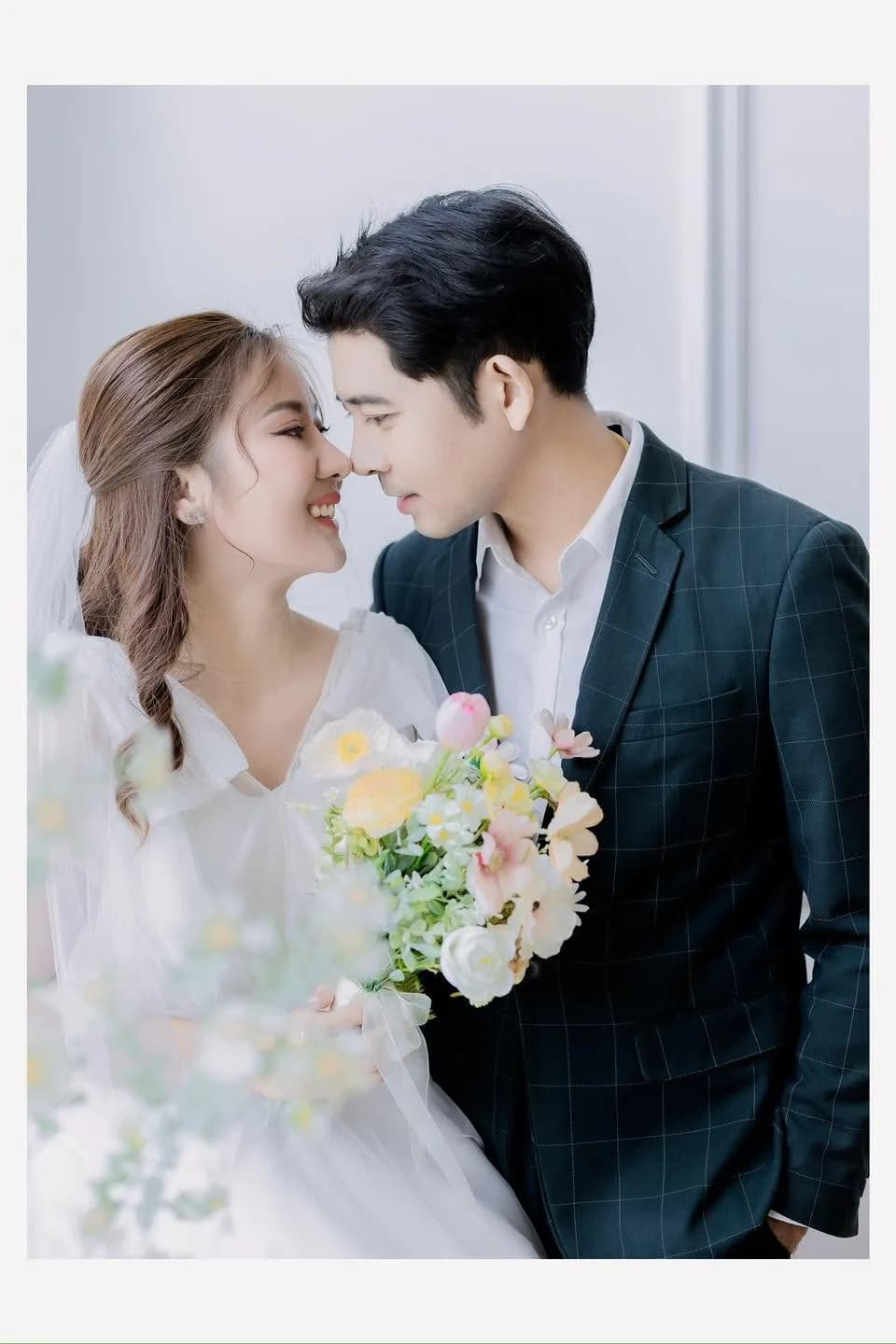 คู่บ่าวสาวยืนใกล้กันจนหน้าผากเกือบแตะกัน โดยเจ้าสาวถือช่อดอกไม้