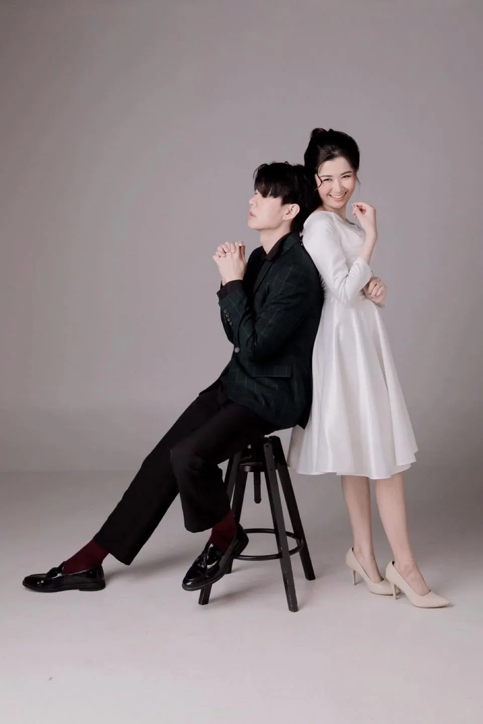 คู่รักในชุดสีขาวและสูทสีดำถ่ายภาพคู่กับเก้าอี้ในสตูดิโอ