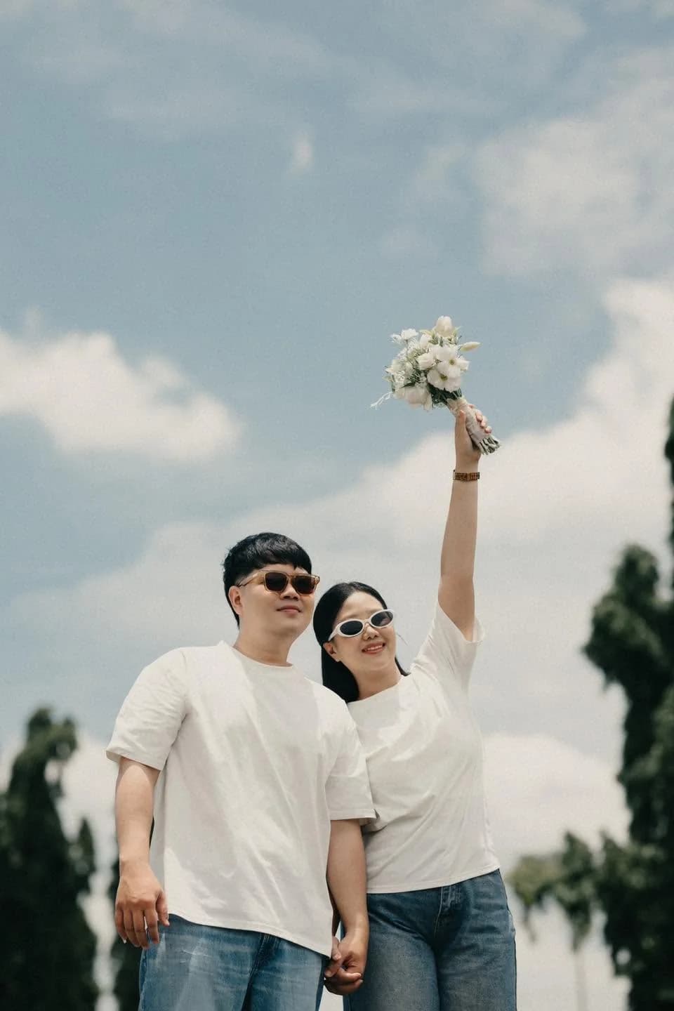 คู่รักชุดลำลองยืนกลางแจ้ง ชูช่อดอกไม้ใต้ท้องฟ้าสีฟ้า