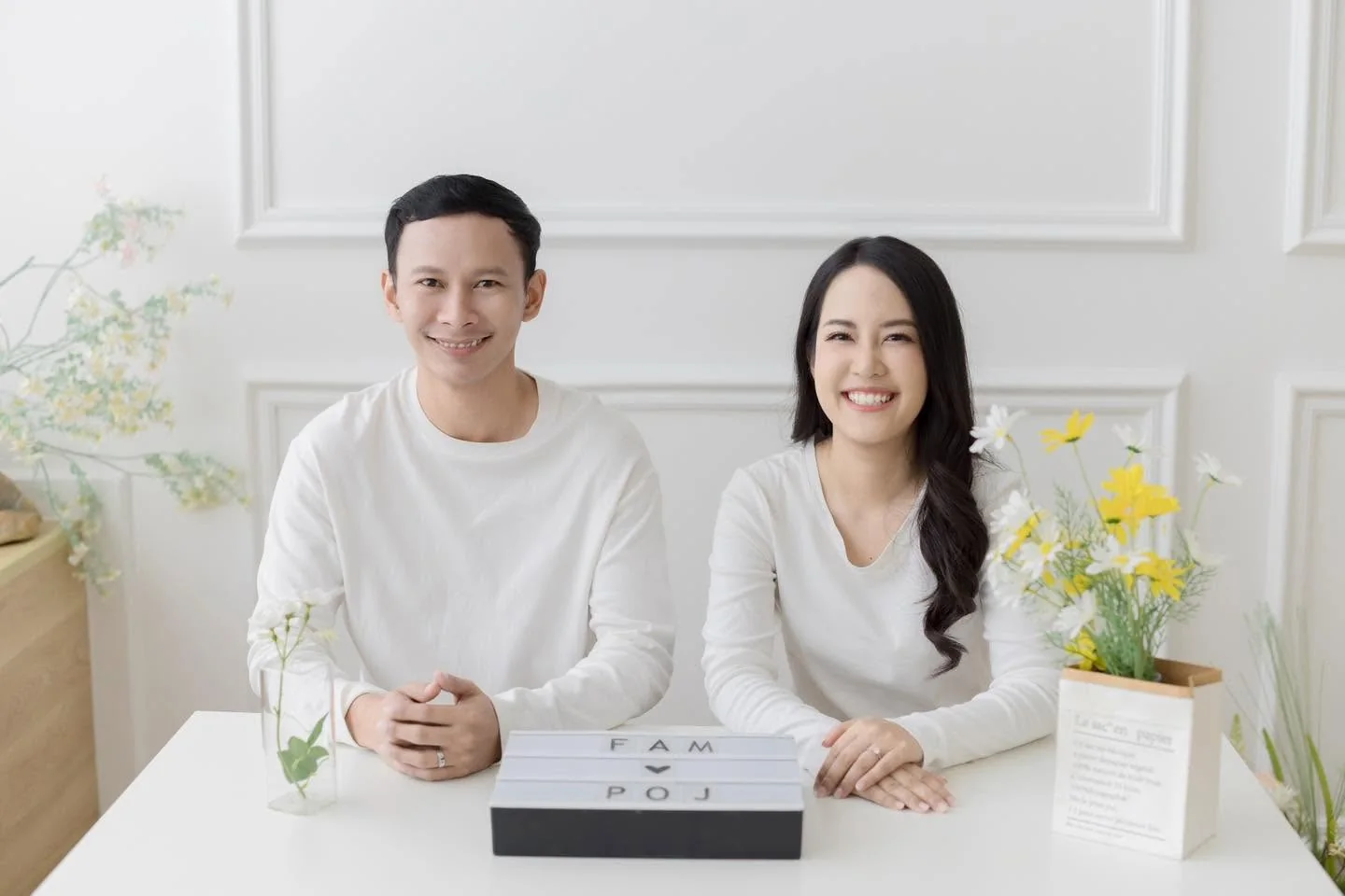 คู่รักสวมเสื้อสีขาวนั่งยิ้มด้วยกันในสตูดิโอ