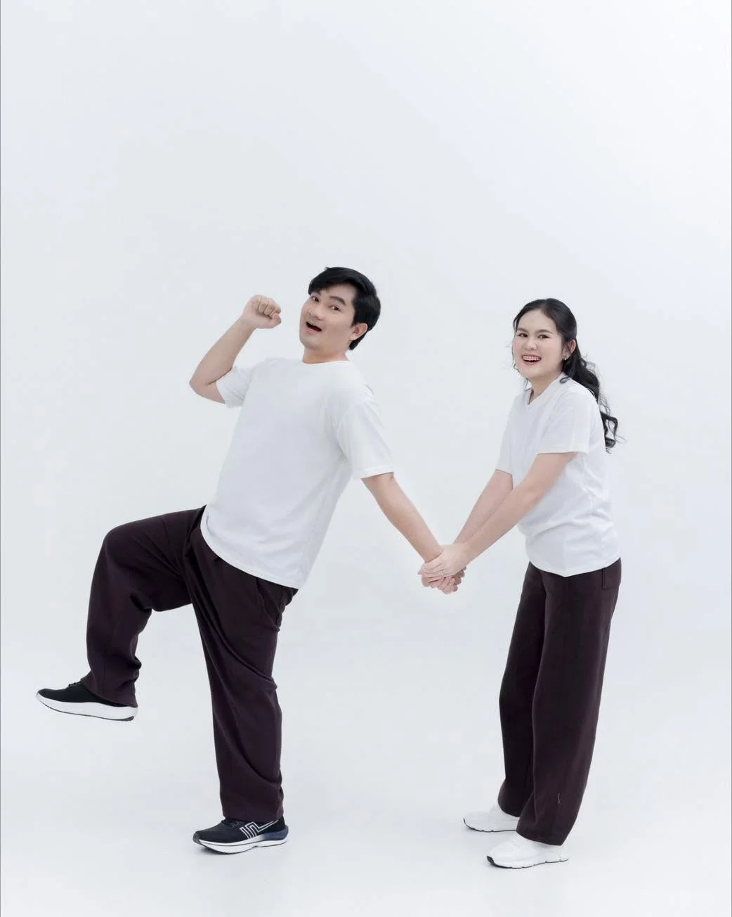คู่รักในเสื้อยืดสีขาวจับมือกันถ่ายภาพท่าทางสนุกสนาน